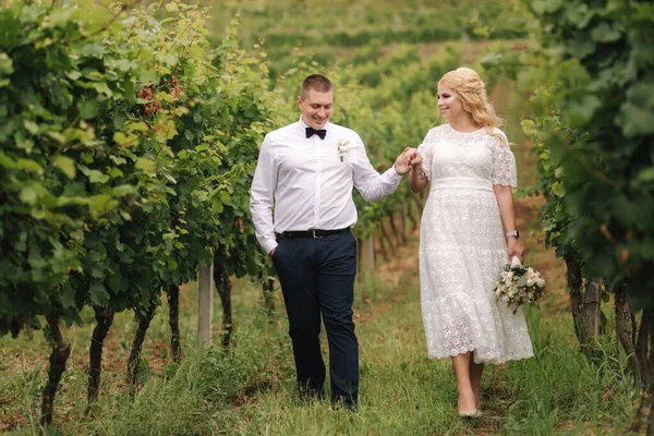 Mariée et fiancée marchant dans le vignoble le jour de leur mariage. Cheveux blonds femme en robe blanche tenir bouquet de mariage dans les mains — Photo