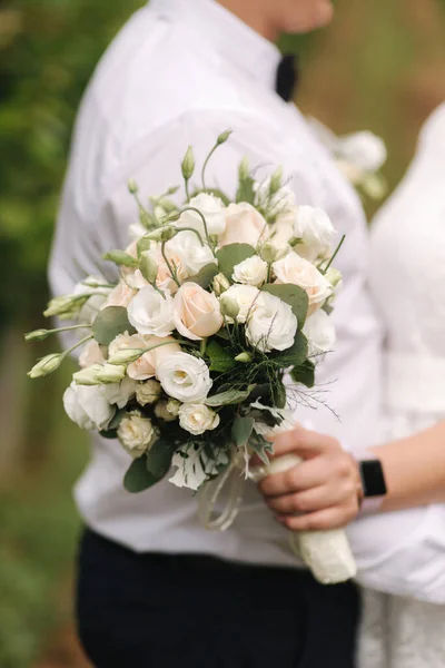 Noivo e noiva andando na vinha em seu dia de casamento. Mulher de cabelo loira em vestido branco segurar buquê de casamento nas mãos. Close up de buquê — Fotografia de Stock