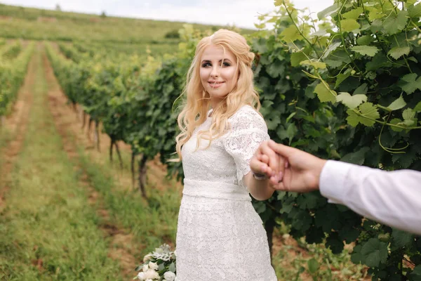 Жених и невеста идут в виноградник в день своей свадьбы. Светлые волосы женщина в белом платье держать свадебный букет в руках — стоковое фото