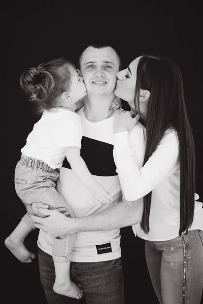 Close up portrait of mom and dad kiss daughter. Studio photosession. Black background. Black and white photo