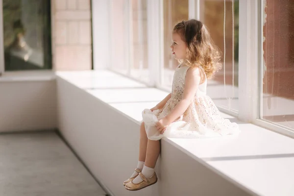 Cute little girl three year old in dress posing for photograper in studio. Beutiful little girl sits on windowsill — Stock Photo, Image