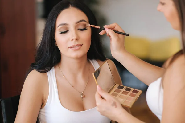 Make-up malíř aplikuje oční stíny, perfektní večerní make-up. Krásná brunetka dívka s perfektní pletí ve studiu — Stock fotografie