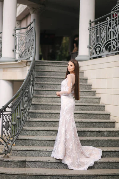 Gorgeous model in wedding dress stand on stair by big restaurant — Stock Photo, Image