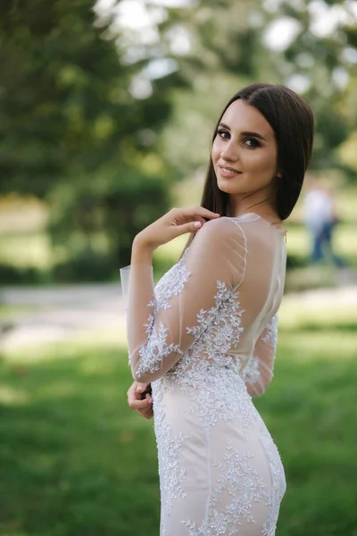 Magnifique jeune femme en robe de mariée stan en plein air devant les arbres verts — Photo