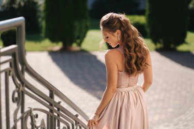 Çekici bir genç kadın, harika bir akşam elbisesi ve kıvırcık saçlarıyla fotoğrafçıya poz veriyor.