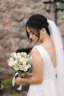 Zarif gelin, buketi taş duvarın önünde elinde tut.