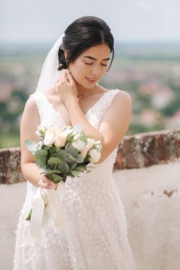 Güzel gelin, şehir manzarası altında buket ve gülümsemeyle duruyor.