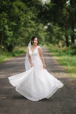 Zarif gelin parkta yürüyor ve etrafında dönüyor. Mutlu gelin, düğün günü