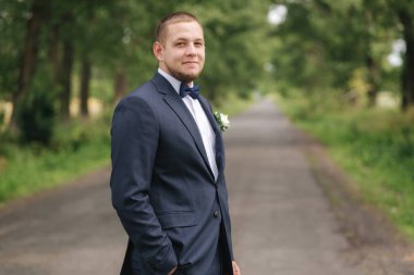 Yakışıklı damat parkta yürüyor ve gülümsüyor.