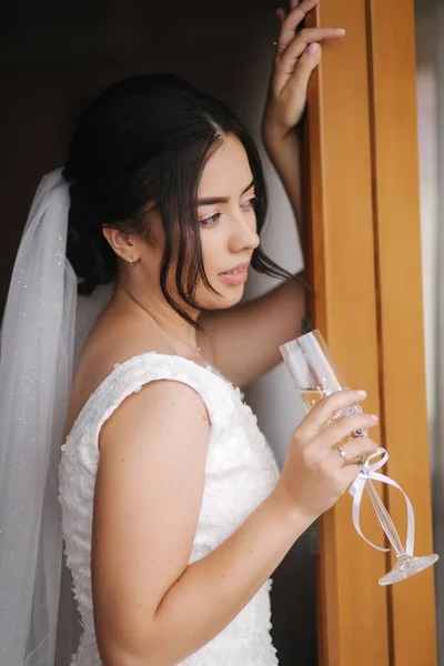 Feliz manhã nupcial com um copo de champanhe. Tender noiva em vestido de noiva por janela — Fotografia de Stock