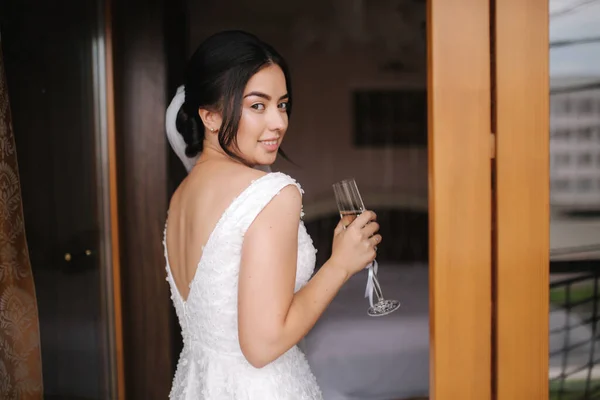 Buon giorno di nozze con un bicchiere di champagne. Sposa tenera in abito da sposa da finestra — Foto Stock