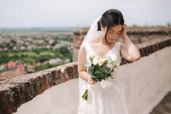 Mooie bruid staan in frind van uitzicht op de stad met boeket en glimlach — Stockfoto