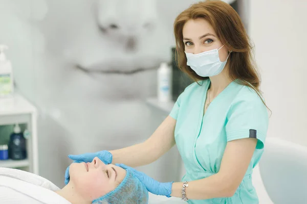 Kosmetikerin macht Gesichtsmassage im Schönheitssalon. Vorbereitungen für die Injektion. Kosmetologe in medizinischer Schutzmaske — Stockfoto