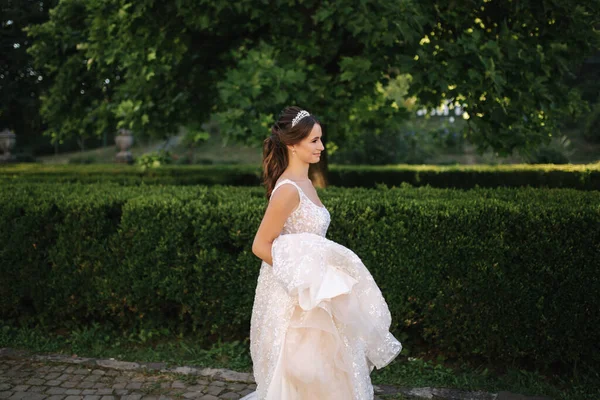 Modelo elegante en vestido de novia posando para fotógrafo al aire libre. Hermosa joven con maquillaje de moda — Foto de Stock