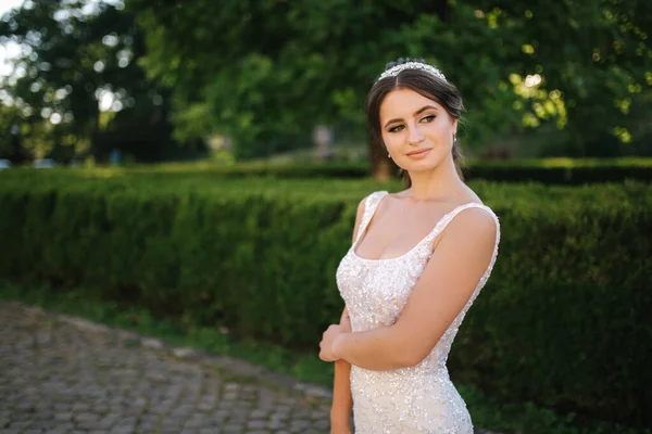 Modelo elegante en vestido de novia posando para fotógrafo al aire libre. Hermosa joven con maquillaje de moda — Foto de Stock