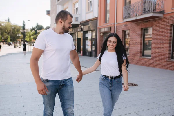 Pareja feliz caminando por el centro de la ciudad. Hombre guapo y mujer atractiva en mierdas blancas —  Fotos de Stock