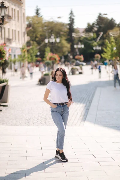 Aantrekkelijke jonge vrouw in wit shirt en jeans wandelen in de stad — Stockfoto