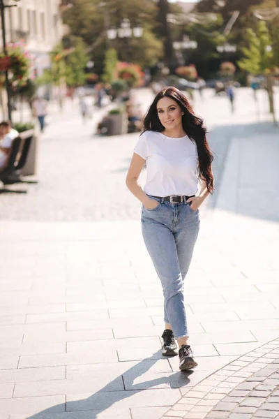 Приваблива молода жінка в білій сорочці і джинсах, що ходять по місту — стокове фото