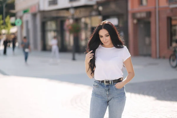 Atractiva joven en camisa blanca y jeans caminando por la ciudad —  Fotos de Stock