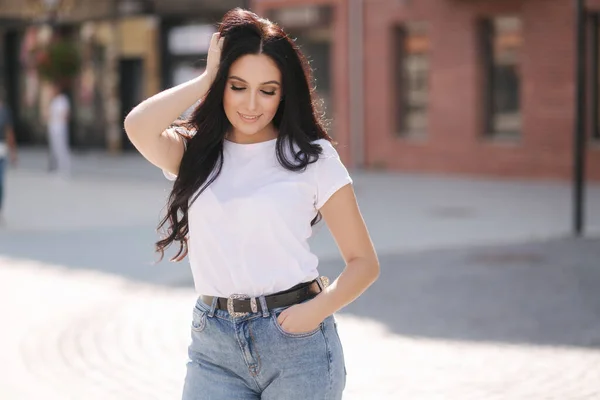 Attraktiv ung kvinna i vit skjorta och jeans promenader i staden — Stockfoto