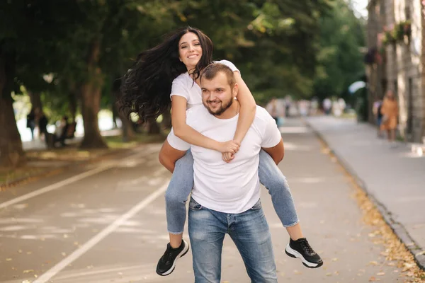 Beautiful gilr climbed on her boyfriend back and hug him. Happy smiled couple spend time in city — Stock Photo, Image