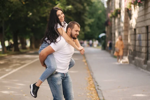 美しいギルーは彼女のボーイフレンドに戻って登り、彼を抱擁しました。幸せなカップルは街で時間を過ごす笑顔 — ストック写真