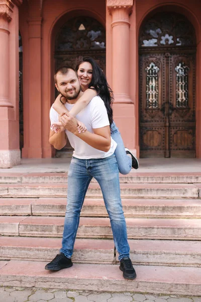 Die schöne Gilr kletterte auf den Rücken ihres Freundes und umarmte ihn. Glücklich lächelndes Paar verbringt Zeit in der Stadt — Stockfoto