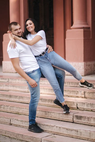 Dos personas rezagadas caminando por la ciudad. Hermosa pareja en mezclilla y camiseta blanca divertirse —  Fotos de Stock