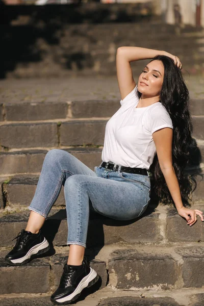 Сексуальна жінка в джинсах сидить на сходах міста. жінка з прекрасною посмішкою — стокове фото