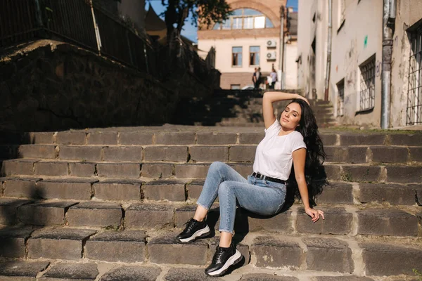 Sexy Frau in Jeans sitzt auf Treppen in der Stadt. Frau mit schönem Lächeln — Stockfoto