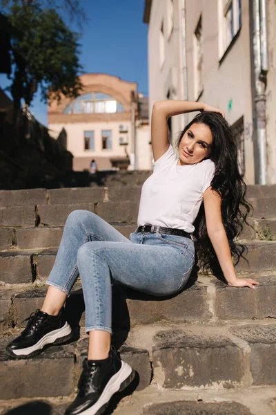 Сексуальна жінка в джинсах сидить на сходах міста. жінка з прекрасною посмішкою — стокове фото