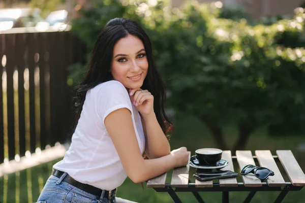Приваблива молода жінка сидить у кафе на відкритому повітрі і п'є каву — стокове фото