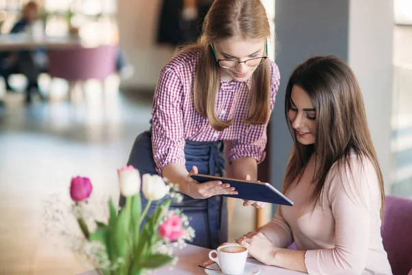 Привлекательная молодая официантка с помощью планшетного компьютера принимает заказ от клиента в кофейне — стоковое фото