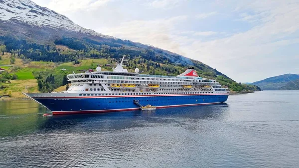 Olden, Norveç - 1 Mayıs 2024: Fred Olsen 'in Norveç fiyordunun içindeki demirleme gemisindeki MV Balmoral yolcu gemisi, orman ve karla kaplı bir dağın arka planına karşı.