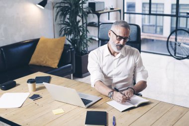 Başarı ve modern coworking ofiste tahta masada çalışırken mobil dizüstü bilgisayar kullanan confidental yetişkin iş adamı.