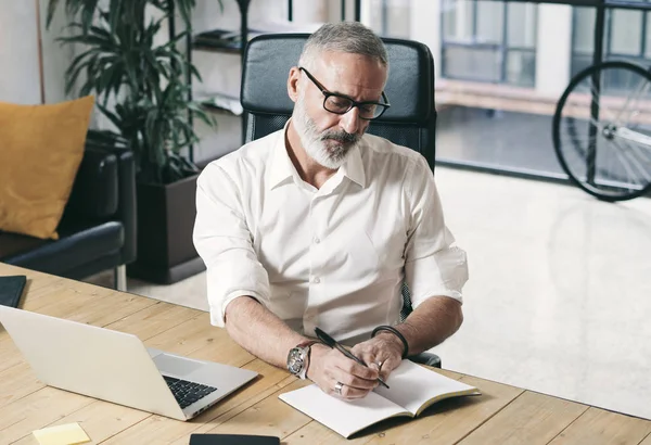 Homme d'affaires adulte attrayant et confident utilisant un ordinateur portable mobile tout en travaillant à la table en bois au bureau de coworking moderne . — Photo