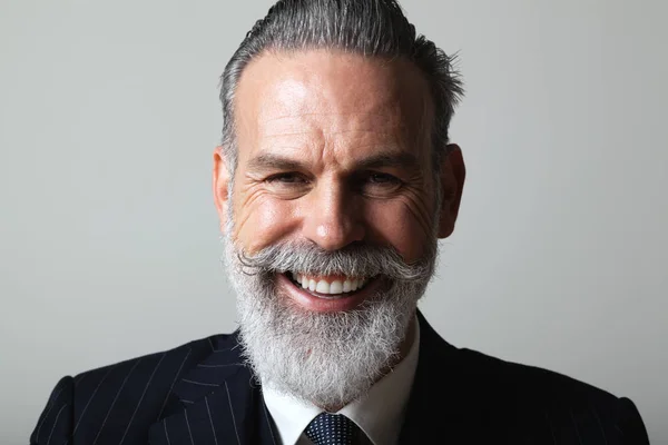 Portrait of happy middle aged bearded gentleman wearing trendy suit over empty gray background. Studio shot, business fashion concept. — Stock Photo, Image