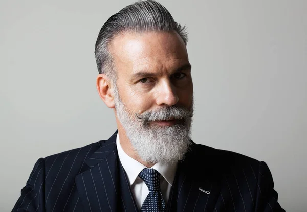 Portrait of pensive middle aged bearded gentleman wearing trendy suit over empty gray background. Studio shot, business fashion concept. — Stock Photo, Image