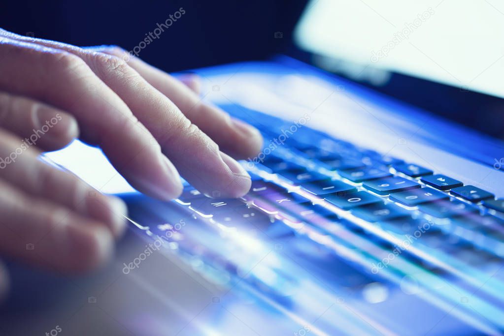 Closeup of male hands typing on laptop keyboard at the office. Visual effects, flares.