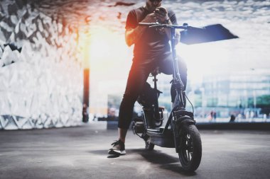 Sakallı dövmeli erkek tarafından şehrin elektrikli scooter sürme sonra smartphone kullanarak güneş gözlüğü.