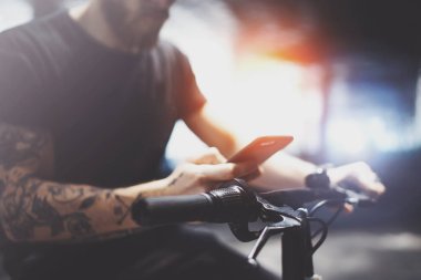 Dövmeli sakallı kaslı adam akıllı telefon elele ve kullanarak app sürme önce şehrin elektrikli scooter tarafından haritalar.