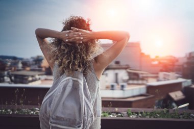 Hansome genç kadın kıvırcık saçları ve rahat kıyafet enjoing güzel şehrin bir günbatımı üzerinde göster.