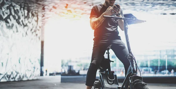Vousatý Tetovaný muž bokovky pomocí mobilního telefonu po koni elektrický Scooter ve městě. Široké — Stock fotografie
