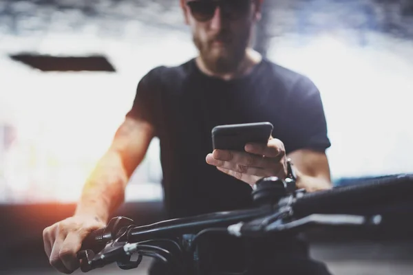 带着胡子的肌肉纹身嬉皮士在太阳镜使用智能手机后骑电动滑板车在城市。创新的交通. — 图库照片