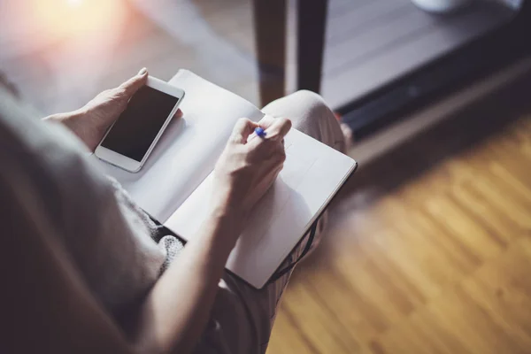 Concept de travail à domicile. Entrepreneur femme d'affaires écrivant et prenant des notes à l'aide de son téléphone mobile et carnet de notes papier — Photo