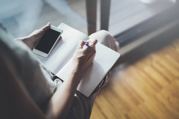 Thuis werken concept. Ondernemer zakenvrouw schrijven en het maken van notities met behulp van haar mobiele telefoon en papier notitie boek — Stockfoto