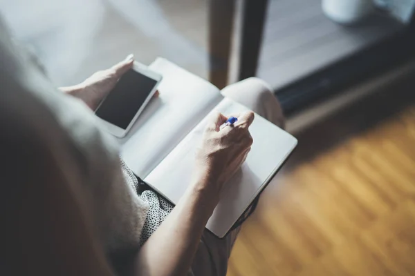 A trabalhar no conceito de casa. Empreendedor mulher de negócios escrevendo e tomando notas usando seu telefone celular e livro de notas de papel — Fotografia de Stock