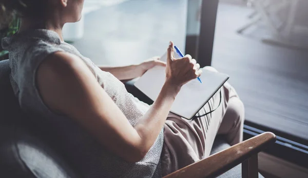 Mujer joven con ropa casual sentada a la mesa en casa y escribiendo en cuaderno. Freelancer trabajando en casa . — Foto de Stock