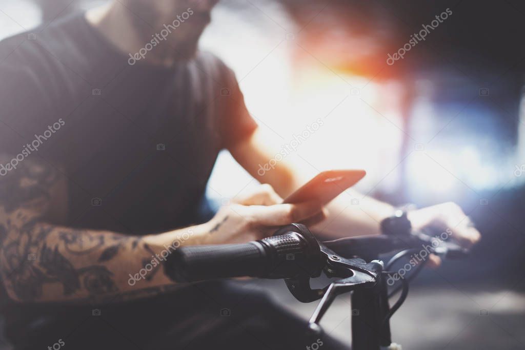 Tattooed bearded muscular man in holding smartphone hands and using maps app before riding by electric scooter in the city.