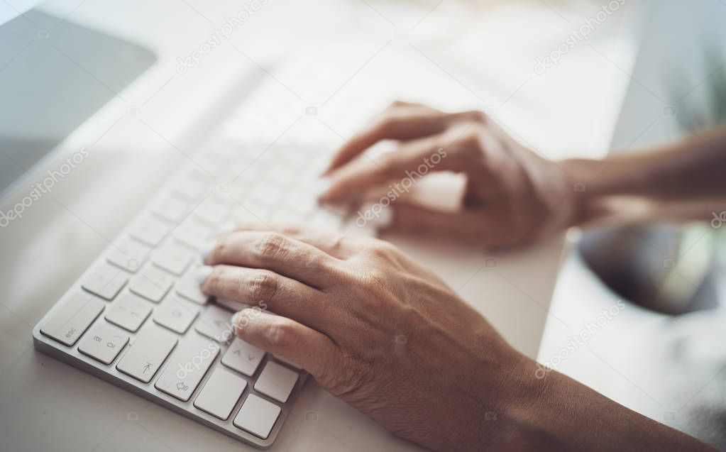 Female hands typing on desktop computer keyboard in modern working place at coworking office.Blurred background.